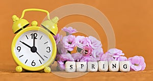 Spring forward, springtime, daylight savings time concept, yellow clock and flowers on orange background