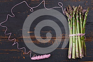 Spring frame with pink thread and green asparagus bunch on the black wooden background. Healthy vegetables for fresh salad