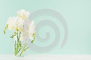 Spring gentle fresh flowers in transparent glass in elegant green mint menthe interior on white wood board, copy space.