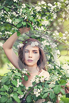 Spring girl face. Pretty young model woman in spring flowers wreath on floral background outdoor