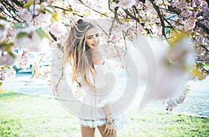 Spring girl in short pink dress enjoying sunny day in garden. Female playing with long gorgeous blond hair, beauty and
