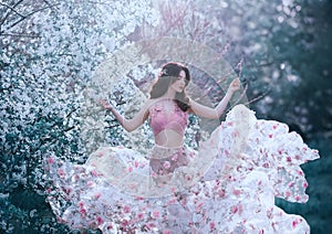 Spring girl with wavy hair dancing dancing on a background of flowering trees. She wears a pink dress with flowers that