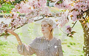 Spring girls in flowers. Beautiful woman in cherry blossom garden on a spring day, flower petals falling from the tree.