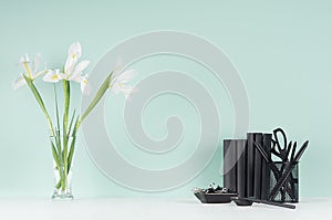 Spring green mint menthe interior of office with black stationery, books, fresh white iris bouquet  in transparent glass vase.