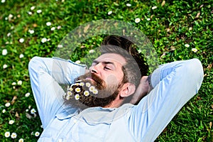 Spring holiday concept. Hipster on happy face lays on grass. Macho with beard and mustache enjoys spring, green meadow