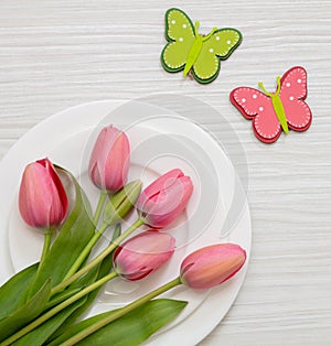 Spring holiday table setting. Fresh tulip on white plate, white wood, overhead