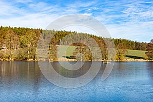 Spring lake in czech countryside. Blue sky, green field and frozen water