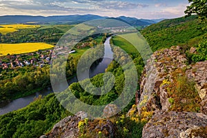 Spring landscape with blooming fields, green meadows and a meandering river in a valley under rocks.