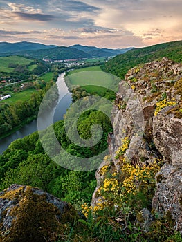 Spring landscape with blooming fields, green meadows and a meandering river in a valley under rocks.