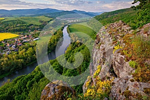 Spring landscape with blooming fields, green meadows and a meandering river in a valley under rocks.