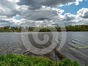 Spring landscape with a lake, fisherman`s fishing on the lake shore, beautiful white clouds, restless lake water