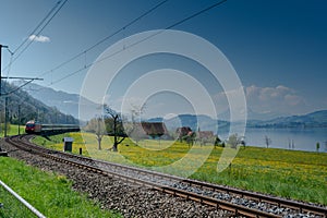Spring landscape with lake and mountains and a train speeding along the tracks in the foreground