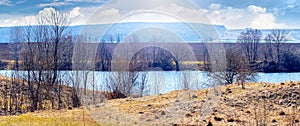 Spring landscape with river, trees by the river and plowed field on a sunny day