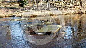 Spring landscape with a small wild river, bare trees without leaves, old board platform in a flooded river