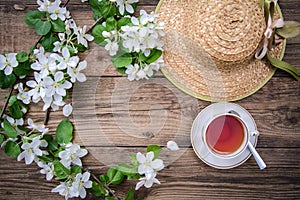 Spring layout with branches of a flowering apple tree, a cup of tea and a straw hat