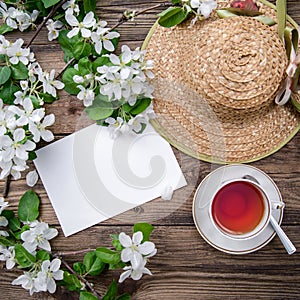 Spring layout with branches of a flowering apple tree, a cup of tea and a straw hat