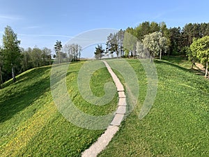 Spring meadow with hiking trail, trees, hill and blue sky