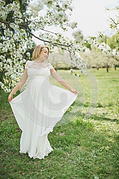 Spring mood, beautiful pregnant woman smell flowering cherry tree, enjoying nature, white floral garden