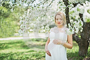 Spring mood, beautiful pregnant woman smell flowering cherry tree, enjoying nature, white floral garden