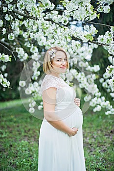 Spring mood, beautiful pregnant woman smell flowering cherry tree, enjoying nature, white floral garden