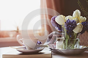 spring morning at home with cup of coffee, book and flowers on white table
