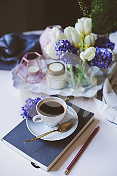 Spring morning at home with cup of coffee, book and flowers on white table