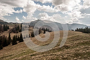 Spring mountais with mountain meadow, trees, hills with small snow fields and blue sky with clouds