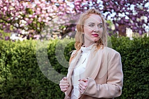 Spring photo of beautiful young girl of European appearance. Strong modern woman in coat in park. Successful business woman