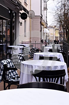 A spring photo of an empty urban cafe terrace with white tablecloths and chakered blankets on the chairs