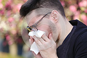 Spring pollen allergy, young man blowing nose in the handkerchie