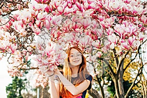 Spring portrait of adorable red-haired preteen kid girl with magnolia flowers