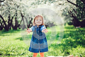 Spring portrait of cute little toddler girl in blue jeans dress walking in blooming park