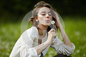 Spring portrait of a girl sitting in a field on the grass among dandelion flowers. Cheerful girl enjoys Sunny spring weather.