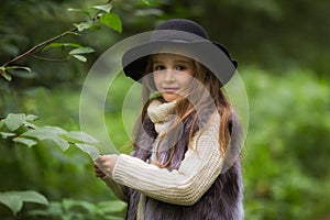 Spring portrait of a little girl.Sweet girl with big brown eyes in a black hat and a fur vest.