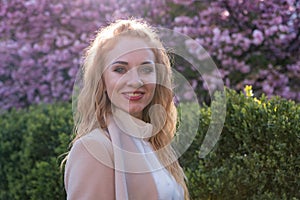 Spring portrait of red-haired beauty in blooming garden with cherry-tree. Young attractive woman with long curly hair in spring