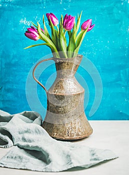 Spring purple tulips in vintage rustic copper jug, blue wall