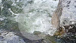Spring river water flowing between two large rocks, closeup detail, slow motion video