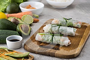 Spring rolls on cutting board with onion among ingredients .