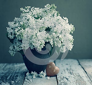Spring romantic bouquet of a white lilac in a vintage old vase and heart with stones