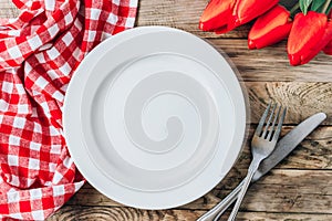 Spring rustic table setting with red tulip, white plate and vintage cutlery on the wooden background