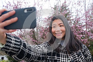 Spring sakura selfie - young happy and cute Asian Korean tourist woman taking self portrait with mobile phone smiling cheerful in