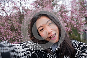 Spring sakura selfie - young happy and cute Asian Korean tourist woman taking self portrait with mobile phone smiling cheerful in