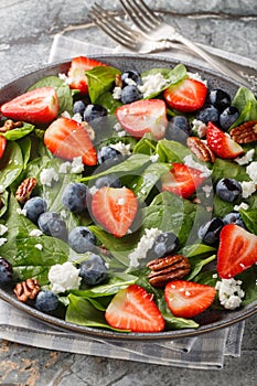 Spring salad of spinach, strawberries, blueberries, goat cheese and pecans close-up in a plate. Vertical