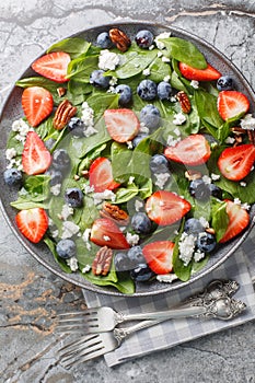 Spring salad of spinach, strawberries, blueberries, goat cheese and pecans close-up in a plate. Vertical top view