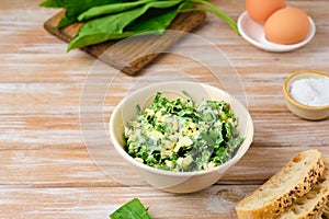 Spring salad of wild garlic and boiled eggs in a ceramic bowl on a wooden background. The use of wild plants for food, the first