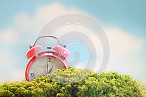 Spring scene of a pink alarm clock under a blue sky