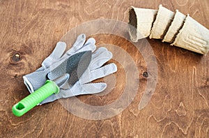 Spring set for seedlings in the garden consisting of gray gloves, a metal shovel and peat pots on a brown wooden