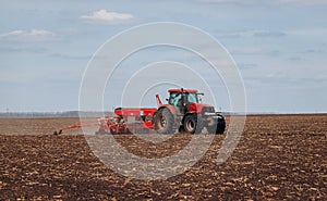 Spring sowing season. Farmer with a tractor sows corn seeds on his field. Planting corn with trailed planter