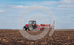 Spring sowing season. Farmer with a tractor sows corn seeds on his field. Planting corn with trailed planter