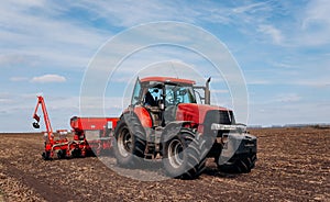 Spring sowing season. Farmer with a tractor sows corn seeds on his field. Planting corn with trailed planter